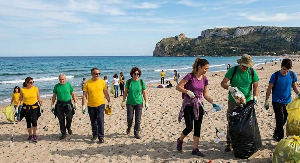 Una distesa di sacchi di rifiuti raccolti dai volontari sulla spiaggia di Giorgino a Cagliari, con il mare e il profilo della costa sarda sullo sfondo.
