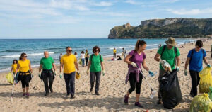 Una distesa di sacchi di rifiuti raccolti dai volontari sulla spiaggia di Giorgino a Cagliari, con il mare e il profilo della costa sarda sullo sfondo.
