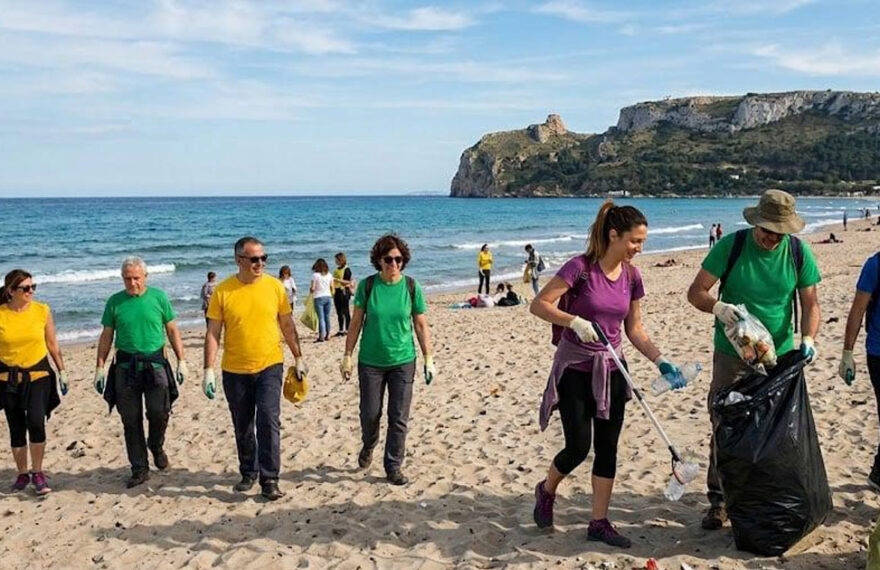 Una distesa di sacchi di rifiuti raccolti dai volontari sulla spiaggia di Giorgino a Cagliari, con il mare e il profilo della costa sarda sullo sfondo.