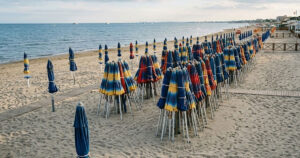 Spiaggia di Ostia deserta con ombrelloni chiusi, simbolo del ritardo della stagione balneare e della crisi dei lavoratori stagionali