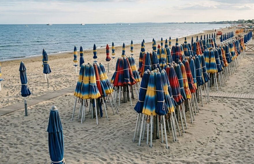 Spiaggia di Ostia deserta con ombrelloni chiusi, simbolo del ritardo della stagione balneare e della crisi dei lavoratori stagionali