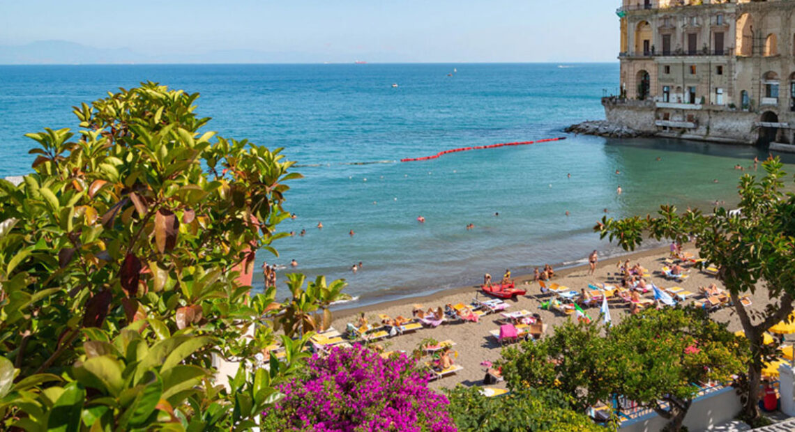Panoramica delle spiagge di Posillipo a Napoli con Palazzo Donn'Anna e il Vesuvio.