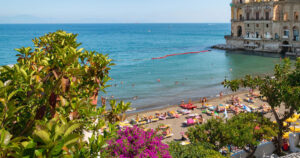 Panoramica delle spiagge di Posillipo a Napoli con Palazzo Donn'Anna e il Vesuvio.