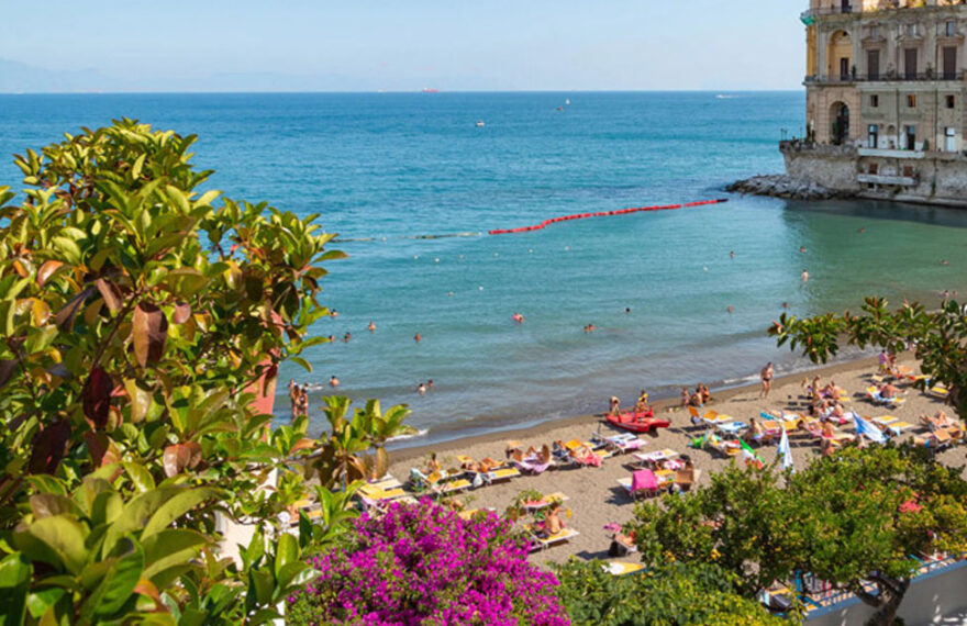 Panoramica delle spiagge di Posillipo a Napoli con Palazzo Donn'Anna e il Vesuvio.