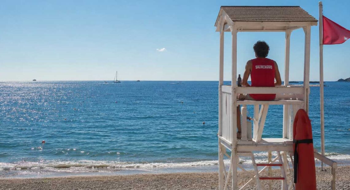 Bagnino di salvataggio seduto in torretta girato di schiena mentre sorveglia il mare aperto.