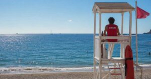 Bagnino di salvataggio seduto in torretta girato di schiena mentre sorveglia il mare aperto.