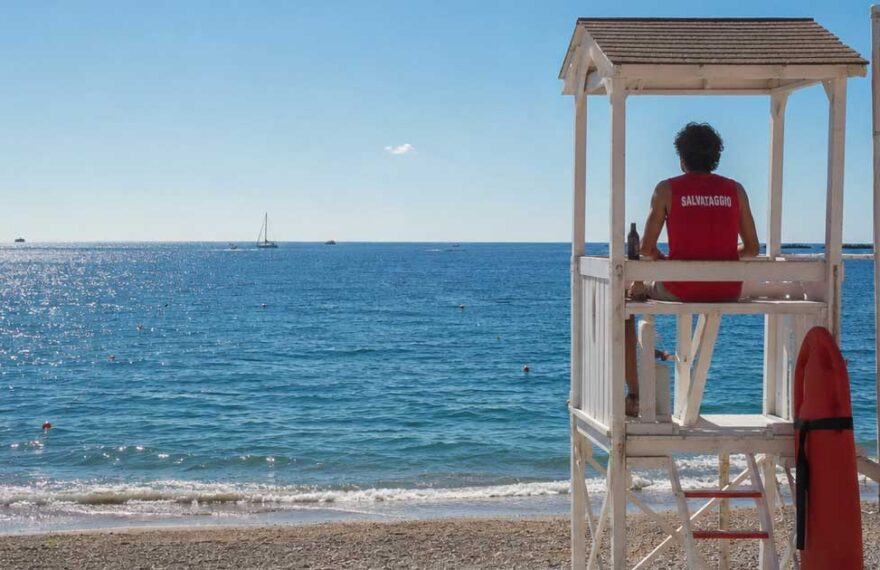 Bagnino di salvataggio seduto in torretta girato di schiena mentre sorveglia il mare aperto.