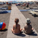 Due bambini seduti sulla passerella di uno stabilimento balneare a Montalto di Castro con giochi da spiaggia e ombrelloni.
