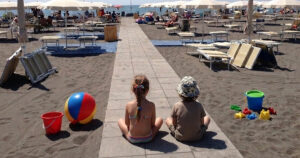 Due bambini seduti sulla passerella di uno stabilimento balneare a Montalto di Castro con giochi da spiaggia e ombrelloni.