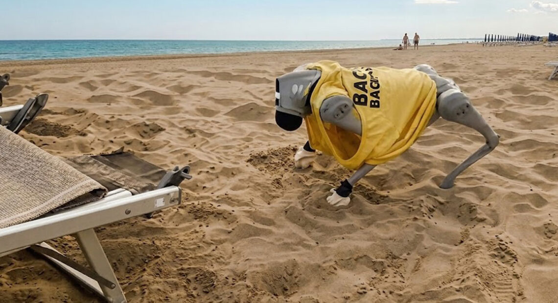 Il cane robot Flipper con la maglietta da bagnino mentre si muove sulla sabbia di una spiaggia a Caorle.