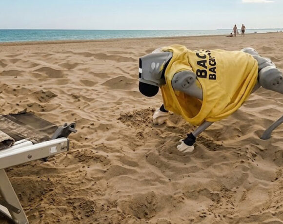 Il cane robot Flipper con la maglietta da bagnino mentre si muove sulla sabbia di una spiaggia a Caorle.