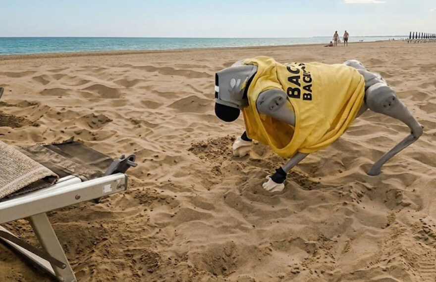 Il cane robot Flipper con la maglietta da bagnino mentre si muove sulla sabbia di una spiaggia a Caorle.