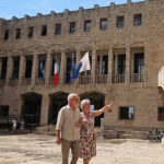 Facciata esterna del Palazzo Comunale di Terracina con bandiere istituzionali esposte sopra l'ingresso e persone nella piazza antistante.