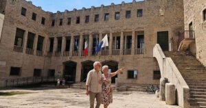 Facciata esterna del Palazzo Comunale di Terracina con bandiere istituzionali esposte sopra l'ingresso e persone nella piazza antistante.