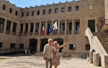 Facciata esterna del Palazzo Comunale di Terracina con bandiere istituzionali esposte sopra l'ingresso e persone nella piazza antistante.