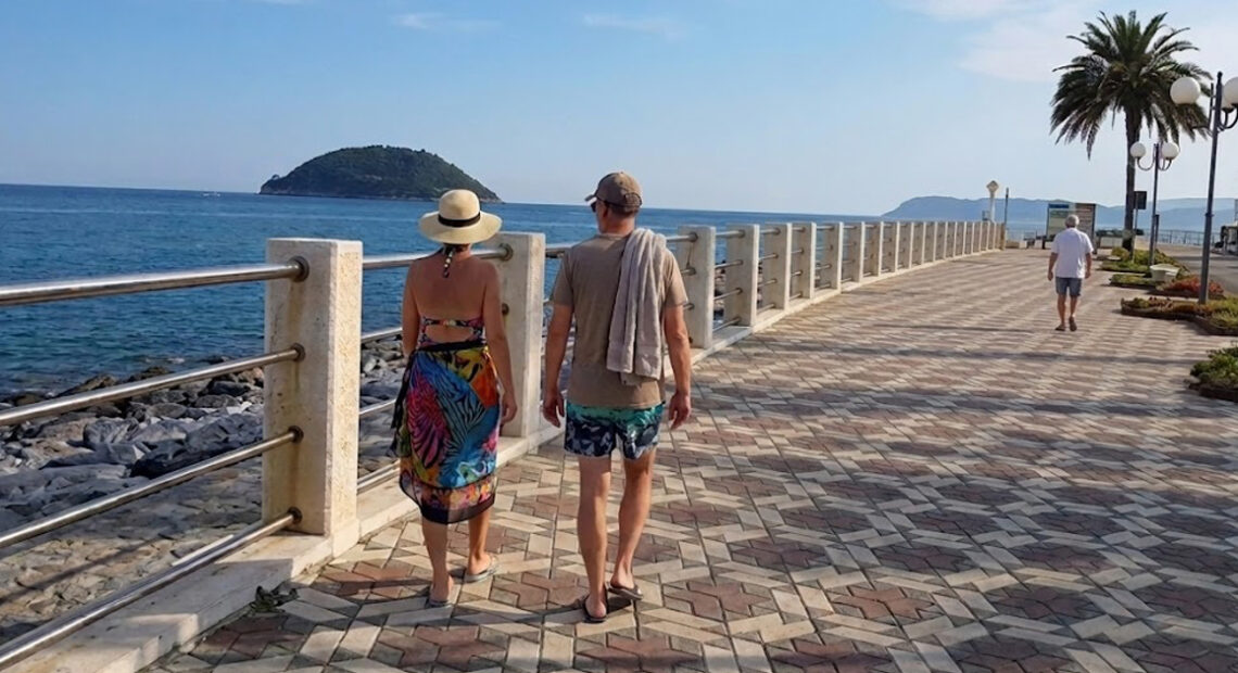 Una coppia di turisti cammina sulla passeggiata lungomare di Albenga di fronte all'isola di Gallinara