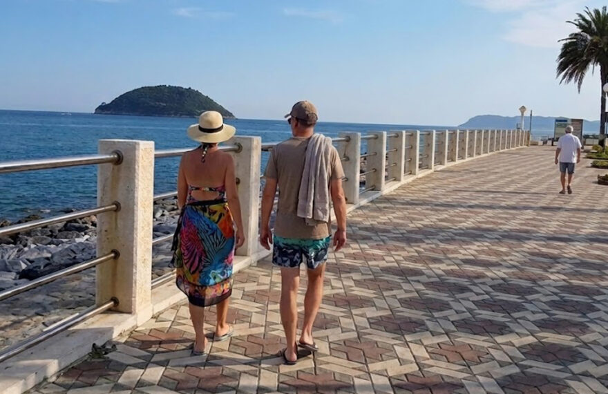 Una coppia di turisti cammina sulla passeggiata lungomare di Albenga di fronte all'isola di Gallinara