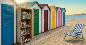 Libreria in legno per il book crossing sulla spiaggia vicino alle cabine colorate di uno stabilimento balneare