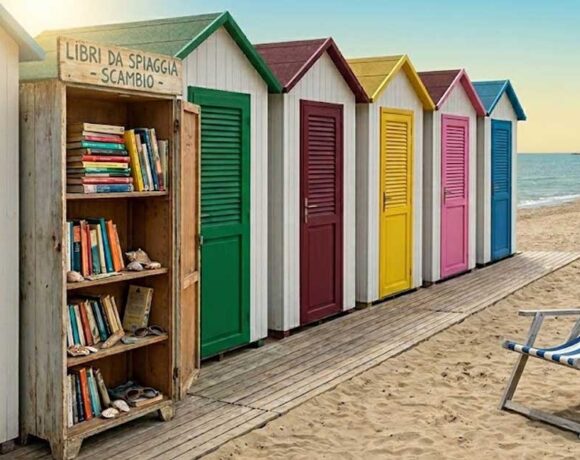 Libreria in legno per il book crossing sulla spiaggia vicino alle cabine colorate di uno stabilimento balneare