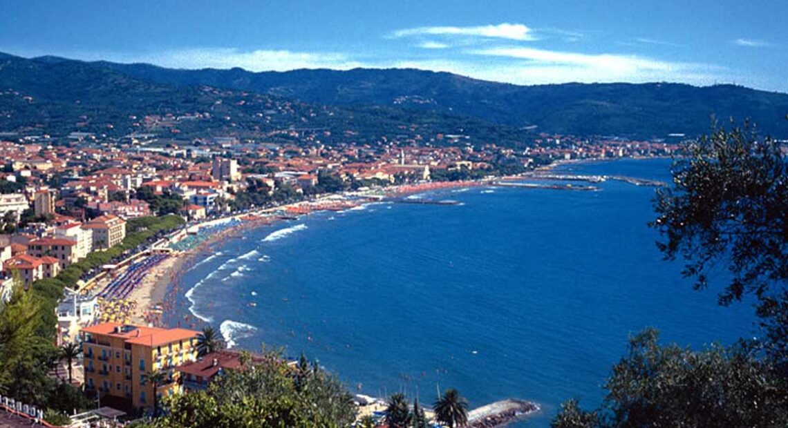 Veduta panoramica dall'alto del golfo di Diano Marina con la linea della spiaggia, gli stabilimenti balneari e le colline ligure sullo sfondo.