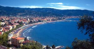Veduta panoramica dall'alto del golfo di Diano Marina con la linea della spiaggia, gli stabilimenti balneari e le colline ligure sullo sfondo.