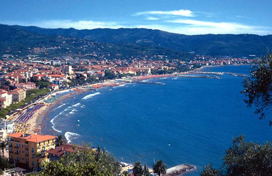 Veduta panoramica dall'alto del golfo di Diano Marina con la linea della spiaggia, gli stabilimenti balneari e le colline ligure sullo sfondo.