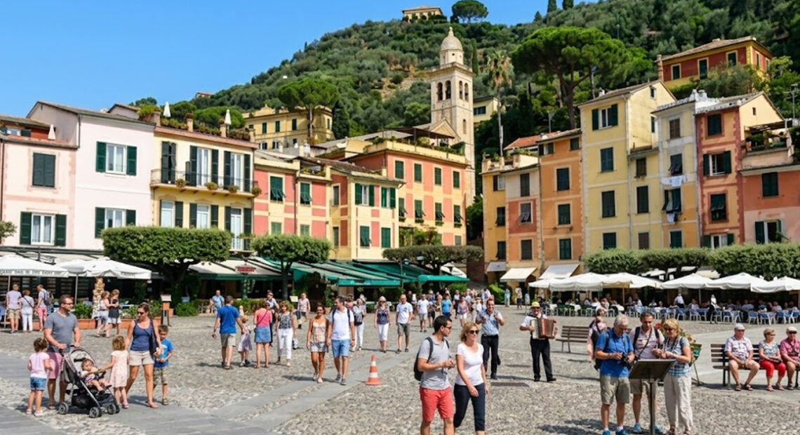 La celebre piazzetta di Portofino affollata di turisti con le tipiche case colorate e la chiesa di San Giorgio sullo sfondo.