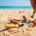 Una mano raccoglie mozziconi di sigaretta dalla sabbia su una spiaggia soleggiata