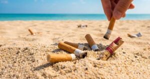Una mano raccoglie mozziconi di sigaretta dalla sabbia su una spiaggia soleggiata