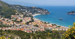 Veduta panoramica dall'alto della costa e del borgo marinaro di Spotorno, in Liguria, con le spiagge e il mare sullo sfondo.