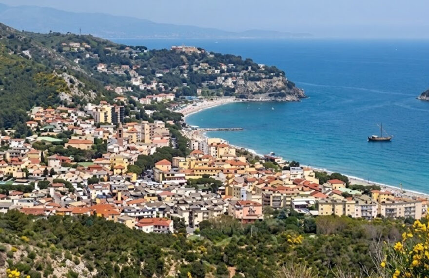 Veduta panoramica dall'alto della costa e del borgo marinaro di Spotorno, in Liguria, con le spiagge e il mare sullo sfondo.
