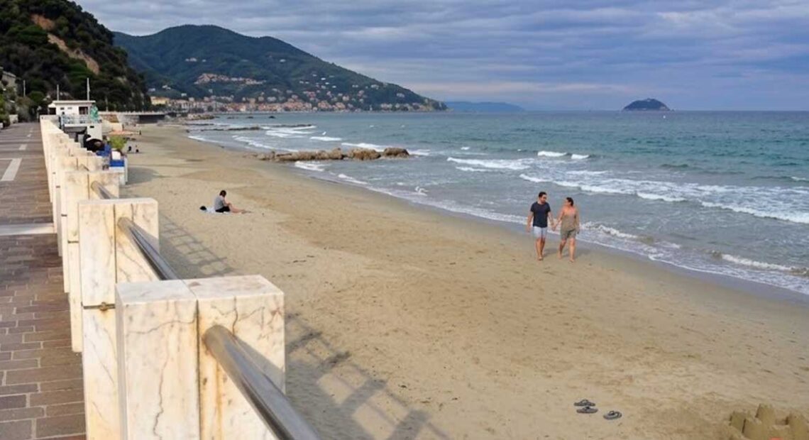 La spiaggia e il lungomare di Laigueglia con bagnanti sulla sabbia e colline sullo sfondo