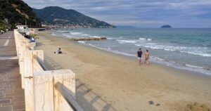 La spiaggia e il lungomare di Laigueglia con bagnanti sulla sabbia e colline sullo sfondo