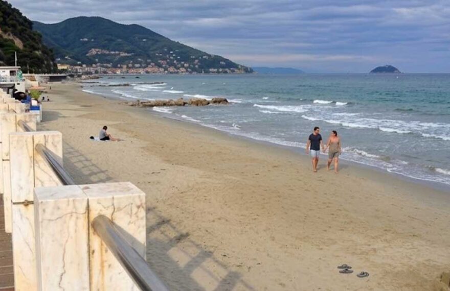 La spiaggia e il lungomare di Laigueglia con bagnanti sulla sabbia e colline sullo sfondo