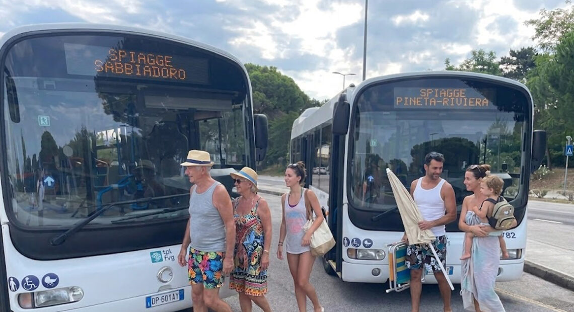 Due autobus di linea TPL FVG a Lignano con display Spiagge Sabbiadoro e Spiagge Pineta Riviera e passeggeri diretti al mare.