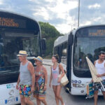 Due autobus di linea TPL FVG a Lignano con display Spiagge Sabbiadoro e Spiagge Pineta Riviera e passeggeri diretti al mare.