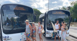 Due autobus di linea TPL FVG a Lignano con display Spiagge Sabbiadoro e Spiagge Pineta Riviera e passeggeri diretti al mare.