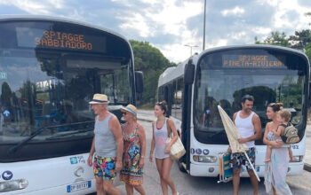Due autobus di linea TPL FVG a Lignano con display Spiagge Sabbiadoro e Spiagge Pineta Riviera e passeggeri diretti al mare.