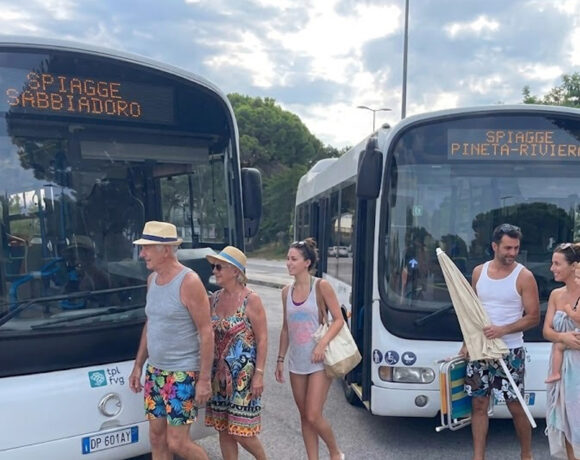Due autobus di linea TPL FVG a Lignano con display Spiagge Sabbiadoro e Spiagge Pineta Riviera e passeggeri diretti al mare.