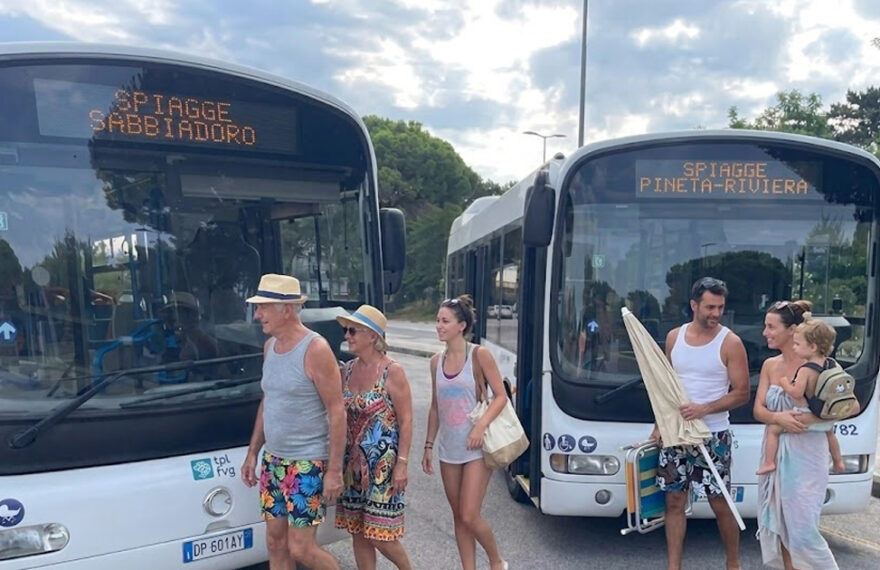 Due autobus di linea TPL FVG a Lignano con display Spiagge Sabbiadoro e Spiagge Pineta Riviera e passeggeri diretti al mare.