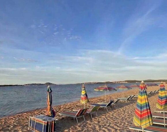 Fila di ombrelloni e lettini sulla sabbia in una spiaggia della Sardegna