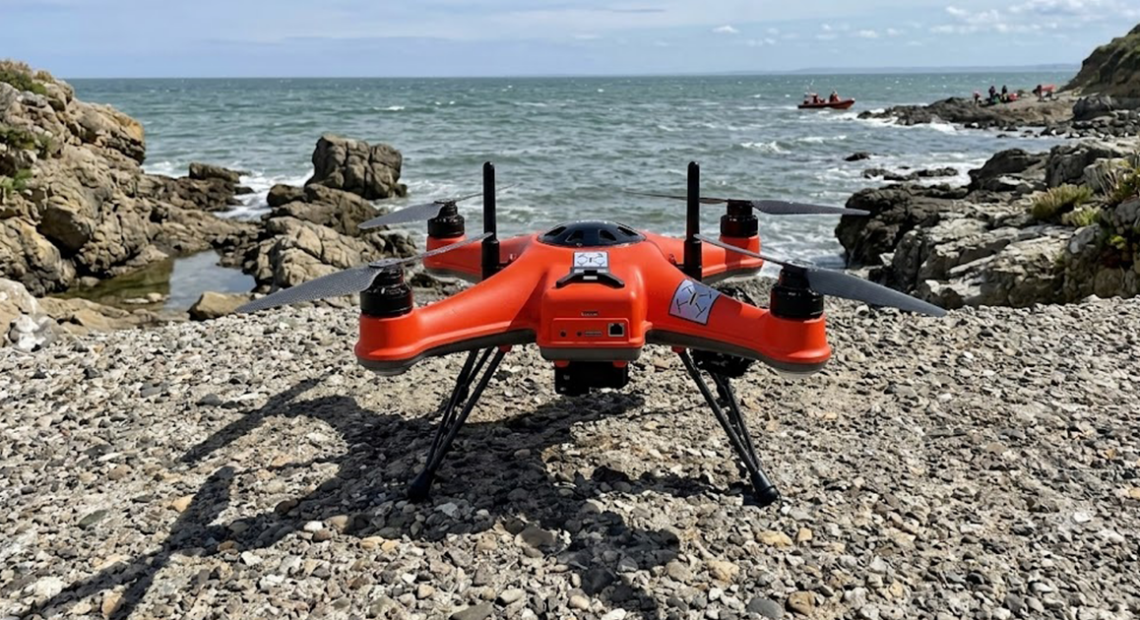 Drone di salvataggio arancione posizionato sulla costa prima dell'intervento in mare.