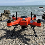 Drone di salvataggio arancione posizionato sulla costa prima dell'intervento in mare.