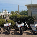 Una fila di biciclette elettriche e-bike nere con cartelli "Servizio Spiaggia" parcheggiate davanti alla sede della Cooperativa Operatori di Spiaggia di Rimini.