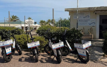 Una fila di biciclette elettriche e-bike nere con cartelli "Servizio Spiaggia" parcheggiate davanti alla sede della Cooperativa Operatori di Spiaggia di Rimini.