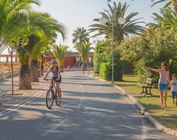 Vista del lungomare di Tortoreto Lido con pista ciclabile, palme, una ciclista e una famiglia a passeggio.