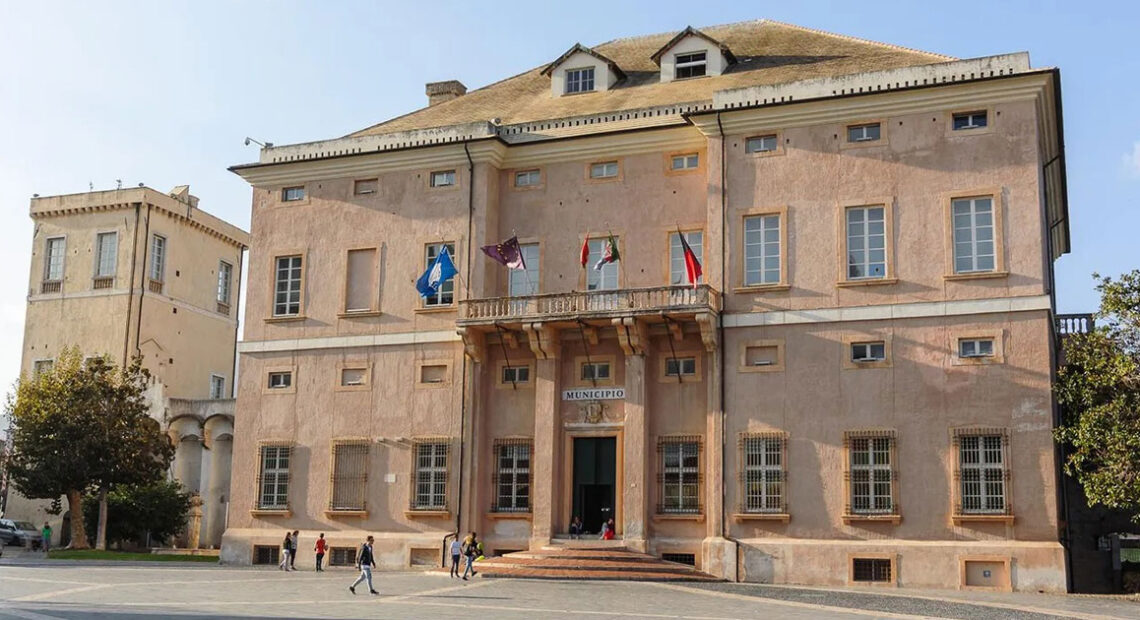 La facciata storica di Palazzo Doria, sede del Comune di Loano, con le bandiere istituzionali sul balcone e la piazza antistante.