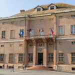 La facciata storica di Palazzo Doria, sede del Comune di Loano, con le bandiere istituzionali sul balcone e la piazza antistante.