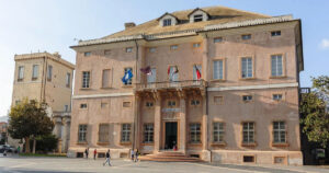 La facciata storica di Palazzo Doria, sede del Comune di Loano, con le bandiere istituzionali sul balcone e la piazza antistante.