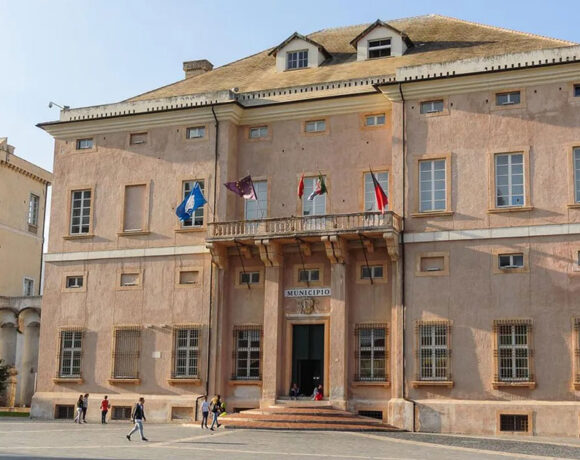 La facciata storica di Palazzo Doria, sede del Comune di Loano, con le bandiere istituzionali sul balcone e la piazza antistante.